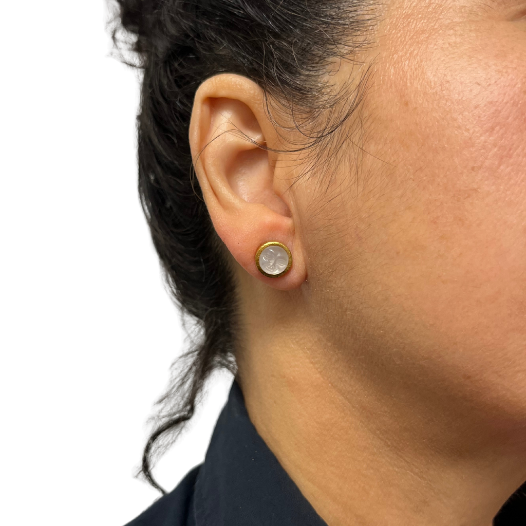 Close-up of an ear wearing a gold earring with a clear gemstone on a white background
