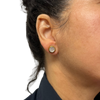 Close-up of an ear wearing a gold earring with a clear gemstone on a white background